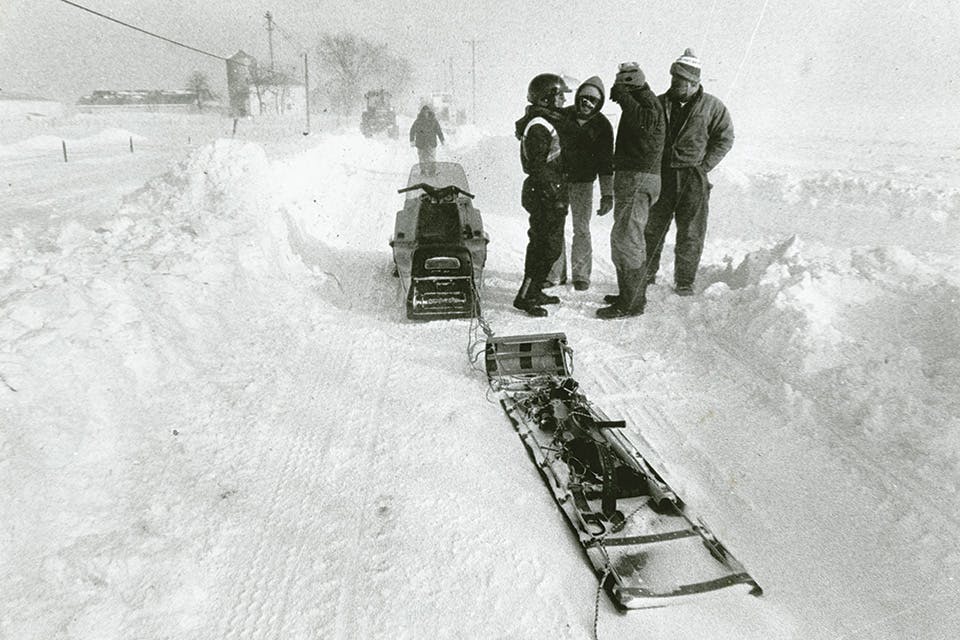 People standing by a snowmobile pulling a toboggan