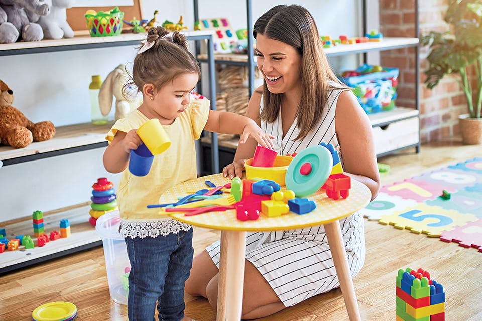 Mom watching daughter play with colorful toys (photo by iStock)