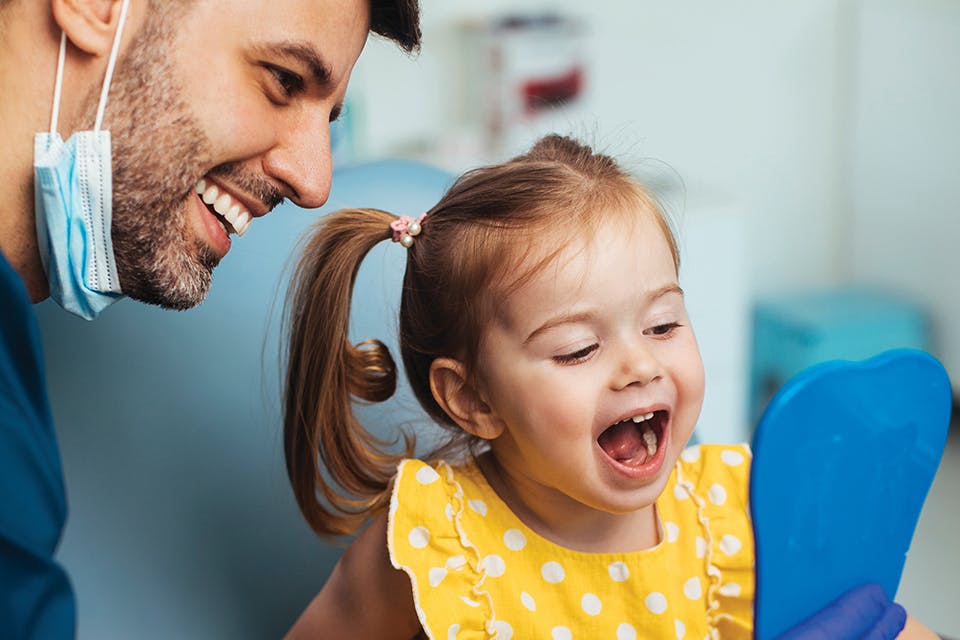 Child looking at teeth in mirror with dentist (photo by iStock)