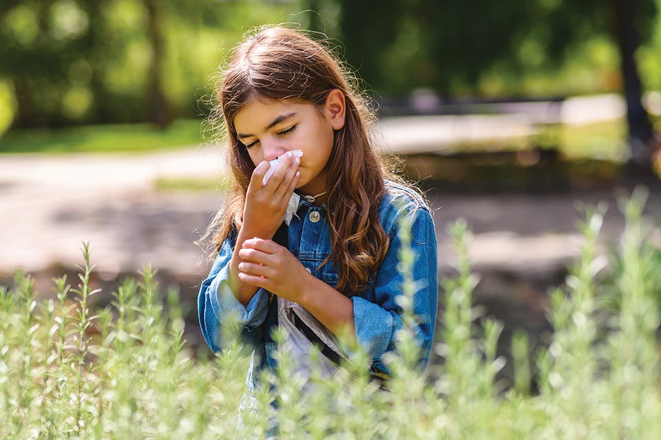 Girl blowing her nose in springtime field (photo by iStock)