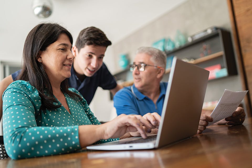 Mom works on laptop computer as dad and son look on (photo by iStock)