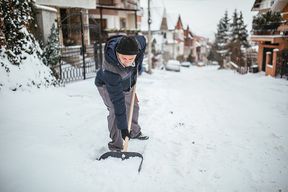 Man shoveling snow on neighborhood street (photo by iStock)