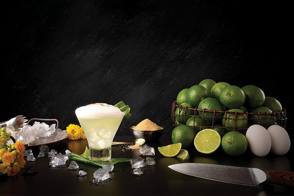 Basket of limes next to ice, sugar and foamy cocktail against black backdrop (photo by iStock)