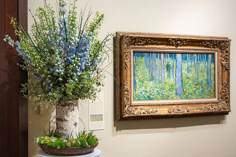 A floral arrangement next to ”Undergrowth with Two Figures” by Vincent van Gogh from Art in Bloom 2025 (photo courtesy of Cincinnati Art Museum)