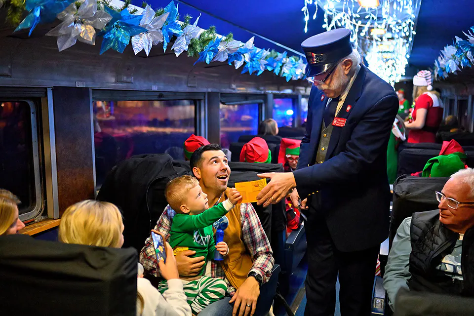 A child hands train ticket to ticket collector on The Polar Express train ride at the Dennison Depot Railroad Museum (photo by Jim Celuch)